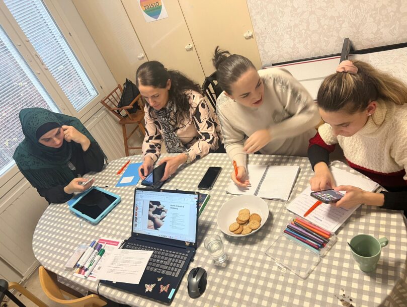 neljä äitiä työskentelee ja juttelee pöydän ääressä