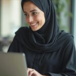 Musliminainen hymyilee tietokoneen takana.