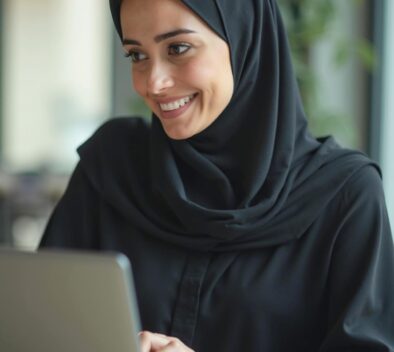 Musliminainen hymyilee tietokoneen takana.