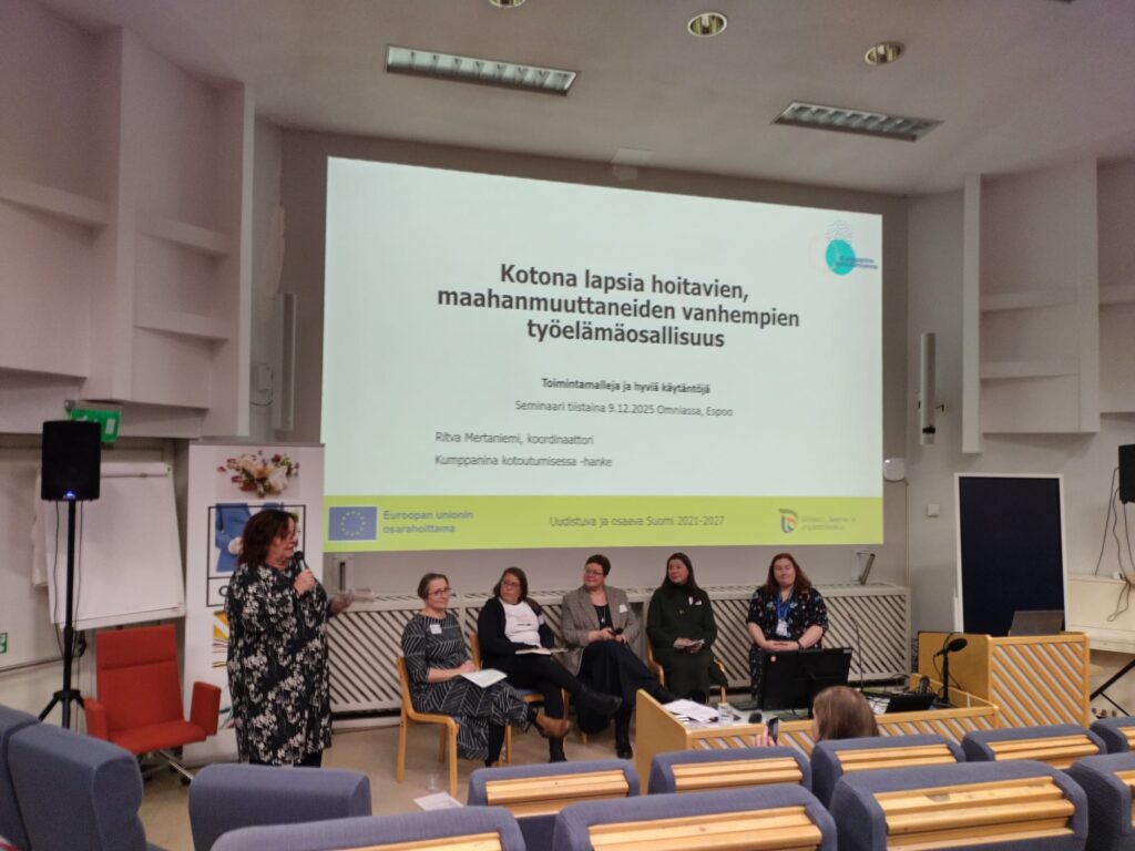 Paneelikeskustelu Ritva Mertaniemi vasemmalla ja viisi panelistia istumassa oikealla, taustalla teksti "Kotona lapsia hoitavien maahanmuuttaneiden vanhempian työelämäosallisuus"