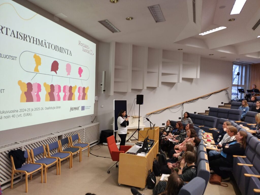 Oikealla auditorioyleisöä, vasemmalla puhujana Sevime Bushi Hoxha ja hänen taustalla "Vertaisryhmätoiminta"-dia